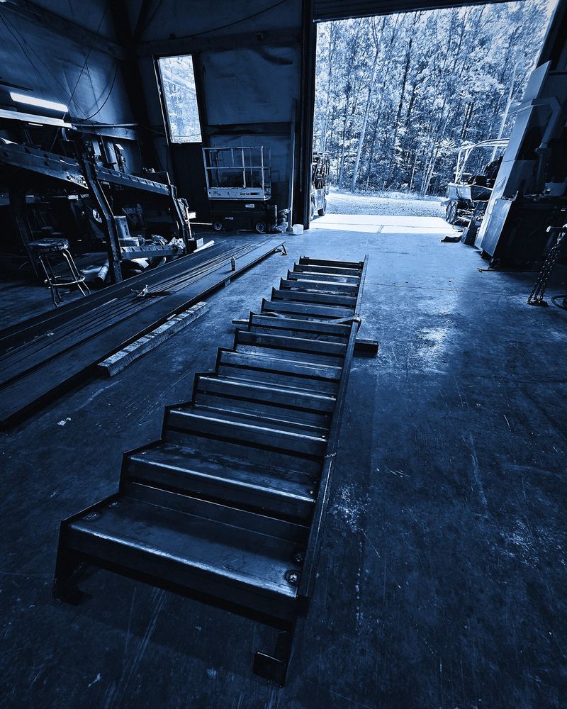 A finished steel stair on the shop floor, pointed at the open bay door