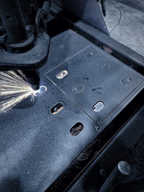 A torch throws sparks while cutting slotted plates from a sheet