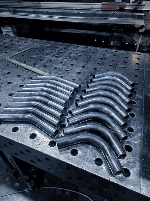 Two fans of bent tube pieces laid out on the fixture table