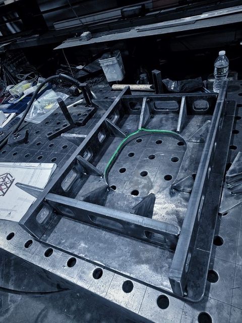 A welded steel frame with gussets and a curved plate on the fixture table