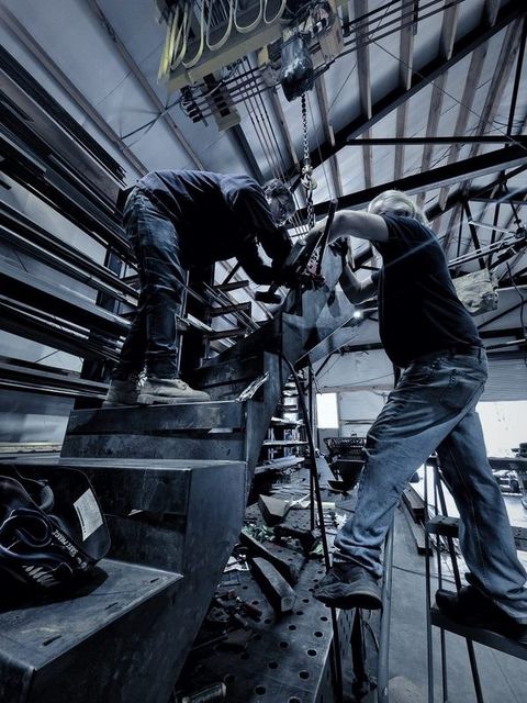 Two men stand up on a curved steel stair, fitting it